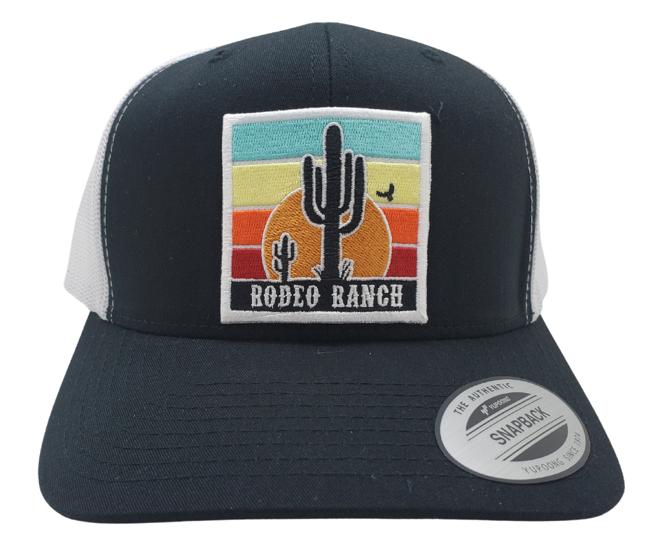 Embrace the thrill of the Rodeo. This Embroidered Trucker Cap features a vibrant desert sun and a towering Cactus. With a Black front, White mesh trucker style, and a snapped adjustable strap, it's ready for any adventure. Visit our Smyrna, TN shop just outside Nashville and claim yours today!