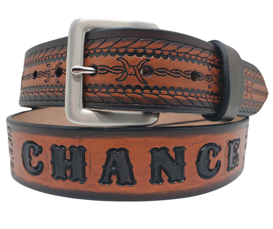 Get ready for an unforgettable adventure with The "Stampede" Name Belt! This one-of-a-kind belt features a 1 1/2" width and is hand-stained with a strip of vegetable tanned leather. The bold design includes a Rope border and Barbwire center pattern, while the solid brass buckle in antique nickel finish adds a touch of ruggedness. Handcrafted at our shop in Smyrna, Tennessee, just outside Nashville.