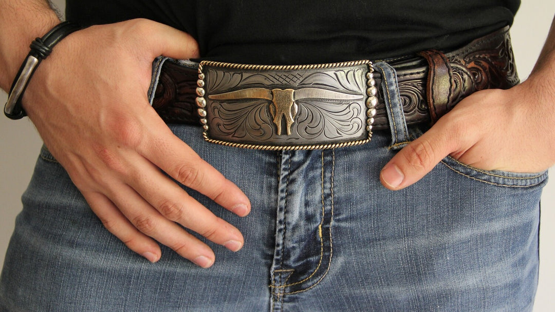 One of our more unique buckles, it has a rectangle shape with a Western scroll design, and a beaded rope edge framing a Longhorn steer. This buckle is made from German Silver (nickel and brass alloy) or iron metal base. Some buckles have motifs made of copper, iron or brass and some are adorned with synthetic stones. Buckle size is Width 5” Height 2” and is available in our Smyrna, TN shop.