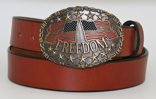 Freedom belt buckle pictured on brown belt-This Freedom belt buckle by And West features 2 American Flags, one flying left and the other toward the right.  Freedom is printed across bottom of buckle and raised stars are featured along the top and bottom of this oval shaped buckle. Barbed wire design surrounds border of buckle. Color is Antique brass look with red and blue flag colors. Available in our online shop and in the retail shop in Smyrna,TN, just outside Nashville. Measures 3" tall by 4" wide.