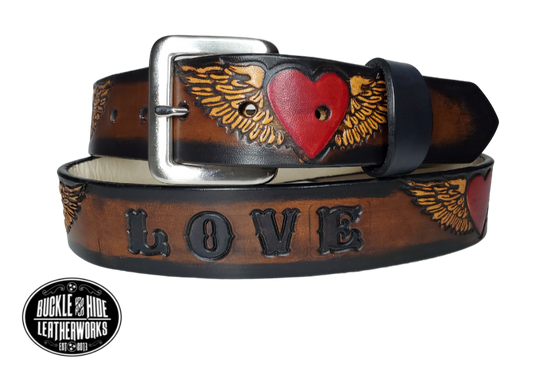 "The Love" is a handmade real leather belt made from a single strip of cowhide shoulder leather that is 8-10 oz. or approx. 1/8" thick. It has hand burnished (smoothed) edges and a Winged Heart pattern. This belt is completely HAND dyed with a multi step finishing technic or you can get in basic earth tones. The antique nickel plated solid brass buckle is snapped in place with heavy snaps.  This belt is made just outside Nashville in Smyrna, TN.