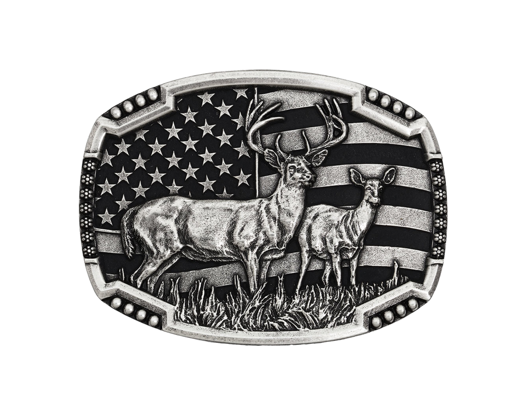 An antiqued silver tone cast buckle with a male and female pair of deer figures standing at attention in the midst of a grassy field. The stars-n-stripes serve as a patriotic backdrop to the animals. The buckle is finished with a smooth wire notched edge with the notches filled with beads. Standard 1.5 inch belt swivel.