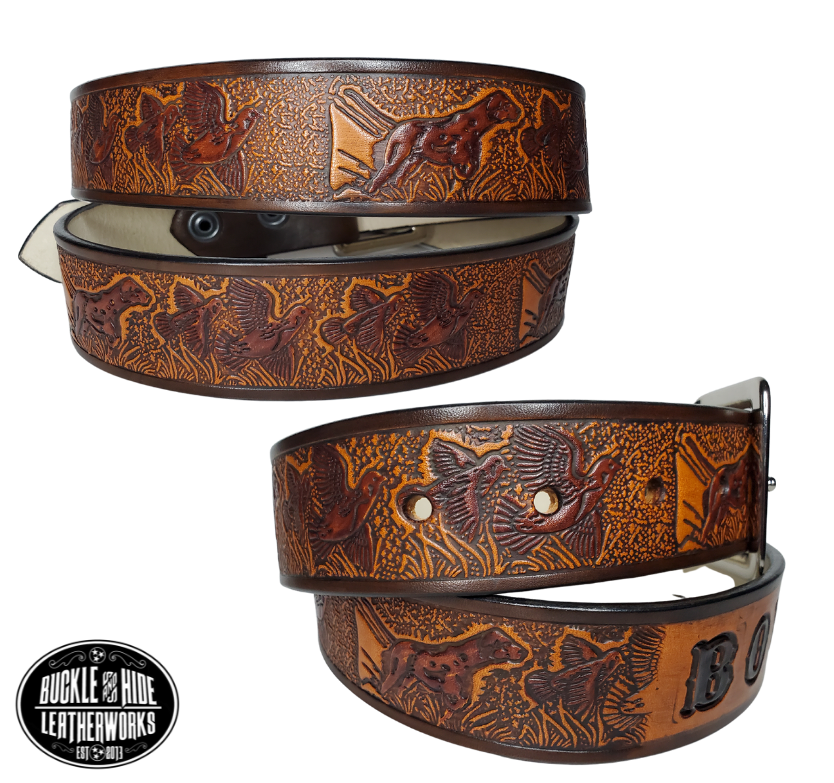 "The Retriever" is a handmade real leather belt made from a single strip of cowhide shoulder leather that is 8-10 oz. or approx. 1/8" thick. It has hand burnished (smoothed) edges and a Bird Hunting scene with a Bird Dog and Quail/Grouse pattern. This belt is completely HAND dyed with a multi step finishing technic. The antique nickel plated solid brass buckle is snapped in place with heavy snaps.  This belt is made just outside Nashville in Smyrna, TN.