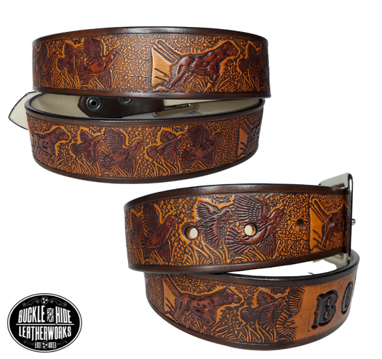 "The Retriever" is a handmade real leather belt made from a single strip of cowhide shoulder leather that is 8-10 oz. or approx. 1/8" thick. It has hand burnished (smoothed) edges and a Bird Hunting scene with a Bird Dog and Quail/Grouse pattern. This belt is completely HAND dyed with a multi step finishing technic. The antique nickel plated solid brass buckle is snapped in place with heavy snaps.  This belt is made just outside Nashville in Smyrna, TN.